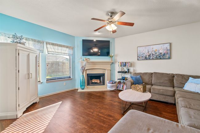 Living area featuring baseboards, a ceiling fan, a fireplace with raised hearth, and dark wood-type flooring | Image 8