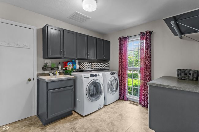 laundry area featuring cabinets, a sink and built-in ironing board. | Image 16