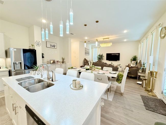 Kitchen with light wood finished floors, appliances with stainless steel finishes, open floor plan, white cabinetry, and decorative light fixtures | Image 8