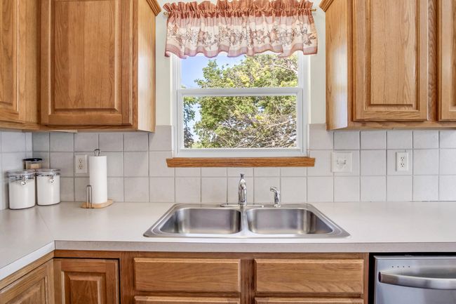 Kitchen with dishwasher, a sink, light countertops, decorative backsplash, and brown cabinetry | Image 12