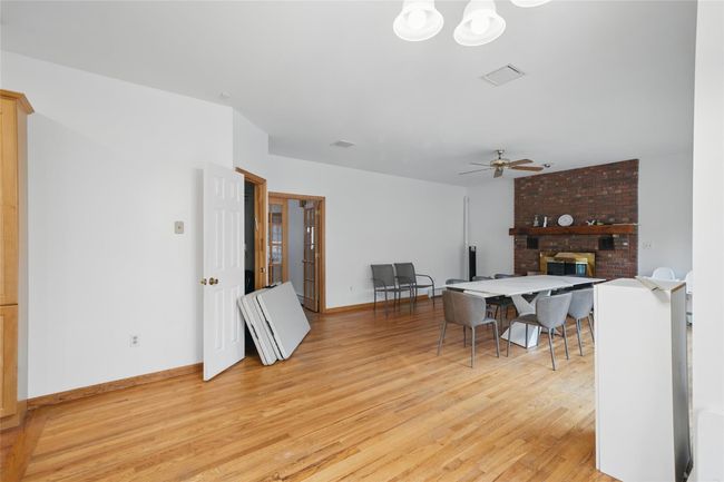 Dining area with light wood finished floors, baseboards, visible vents, a brick fireplace, and ceiling fan | Image 12