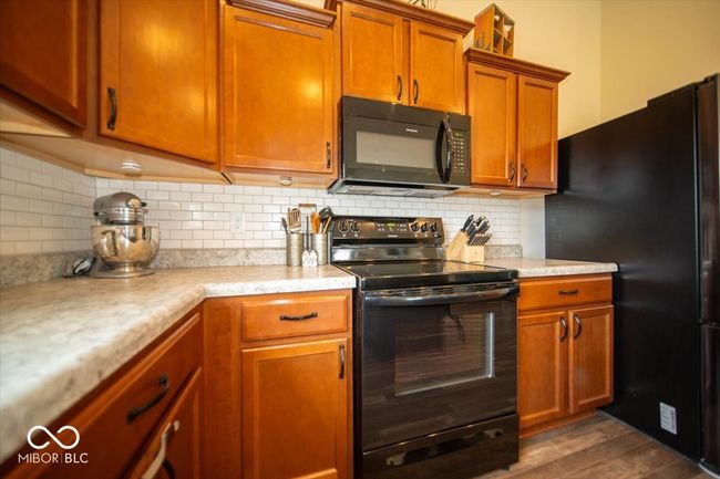 kitchen featuring black appliances, light countertops, dark wood-type flooring, decorative backsplash, and brown cabinets | Image 15