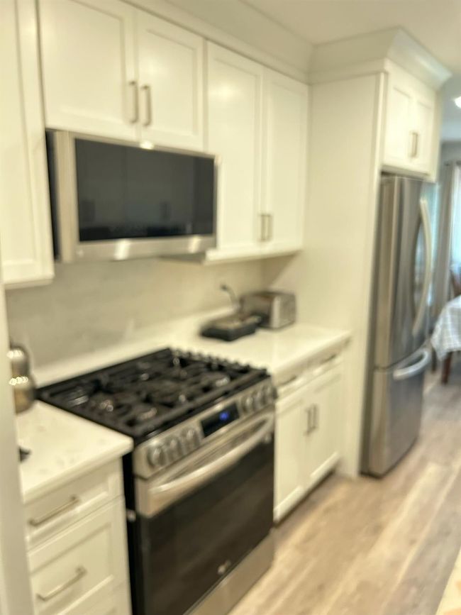 Kitchen featuring appliances with stainless steel finishes, white cabinetry, light countertops, and light wood-type flooring | Image 9