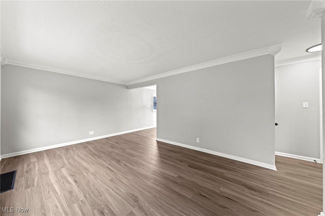 Unfurnished living room with baseboards, visible vents, ornamental molding, and dark wood-type flooring | Image 6