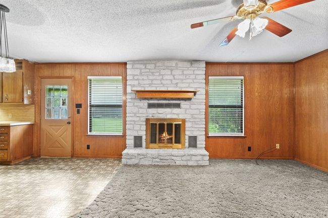 Unfurnished living room featuring wooden walls, a textured ceiling, a ceiling fan, and a fireplace | Image 14