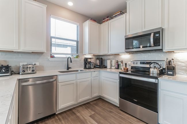 Kitchen featuring appliances with stainless steel finishes, white cabinetry, backsplash, dark wood finished floors, and light stone countertops | Image 13