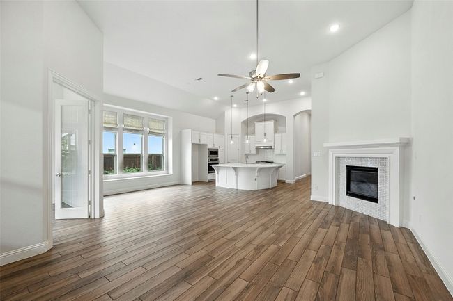 Unfurnished living room with lofted ceiling, a glass covered fireplace, tile floors, a ceiling fan, and arched walkways | Image 14