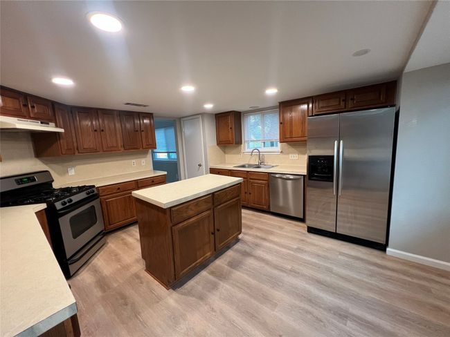 Kitchen featuring appliances with stainless steel finishes, a sink, light countertops, under cabinet range hood, and light wood-style flooring | Image 7