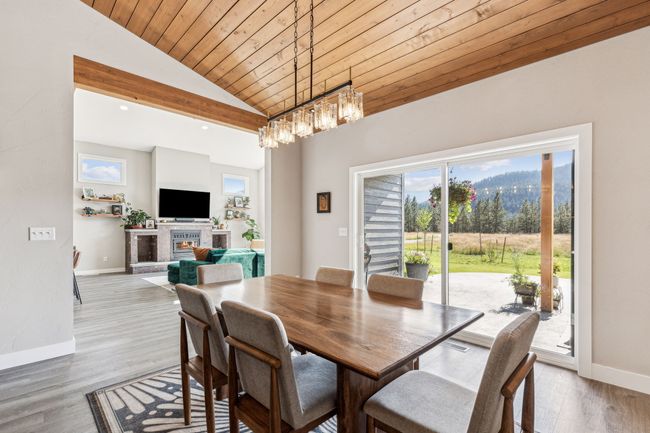 Dining area featuring vaulted ceiling, wooden ceiling, a chandelier, a glass covered fireplace, and baseboards | Image 13