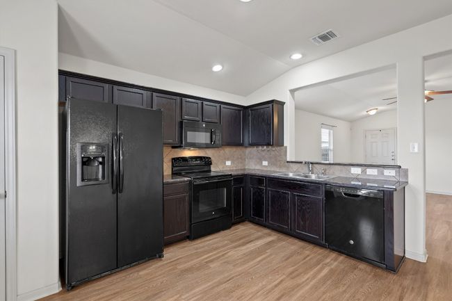 Kitchen with black appliances & dark wood cabinets balance with the lofted ceiling and light wood-style LVP flooring. | Image 6