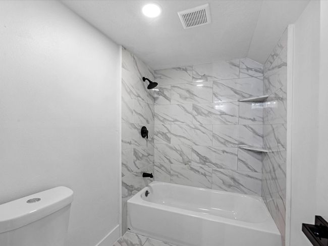 This bathroom features a sleek design with white marble-look tile surrounding a bathtub and shower area. It has modern black fixtures and a simple, clean aesthetic, perfect for a contemporary home. | Image 28