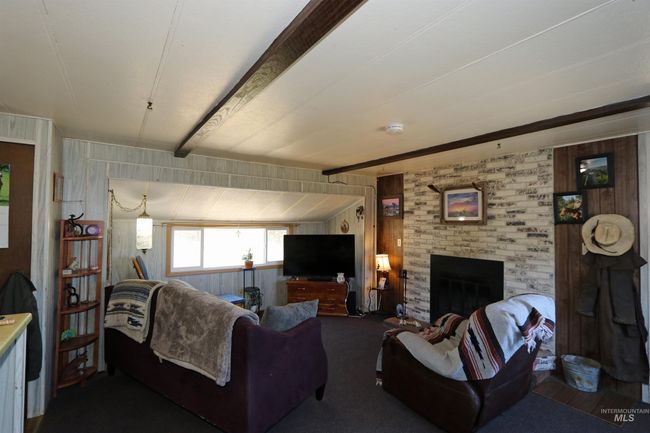 Carpeted living area with beamed ceiling, a brick fireplace, and wood walls | Image 11