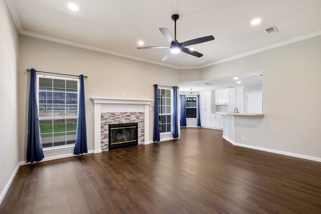 Unfurnished living room featuring ceiling fan, dark wood-style flooring, a fireplace, ornamental molding, and recessed lighting | Image 6