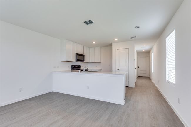 Kitchen with black microwave, white cabinets, light wood-type flooring, a peninsula, and light countertops | Image 4