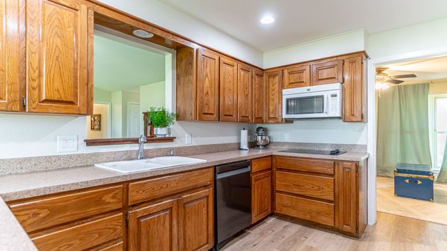 Kitchen featuring light wood-type flooring, white microwave, brown cabinetry, dishwasher, and a sink | Image 13