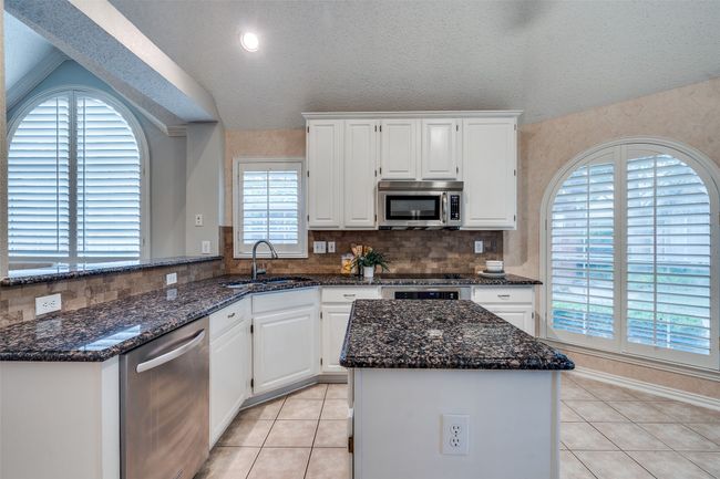 Kitchen featuring stainless steel appliances, a sink, dark stone countertops, white cabinets, and vaulted ceiling | Image 10