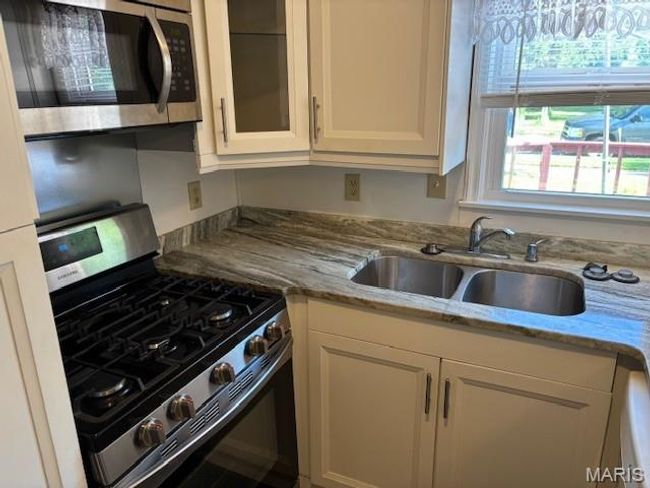 Kitchen featuring appliances with stainless steel finishes, a sink, white cabinetry, glass insert cabinets, and light stone counters | Image 20
