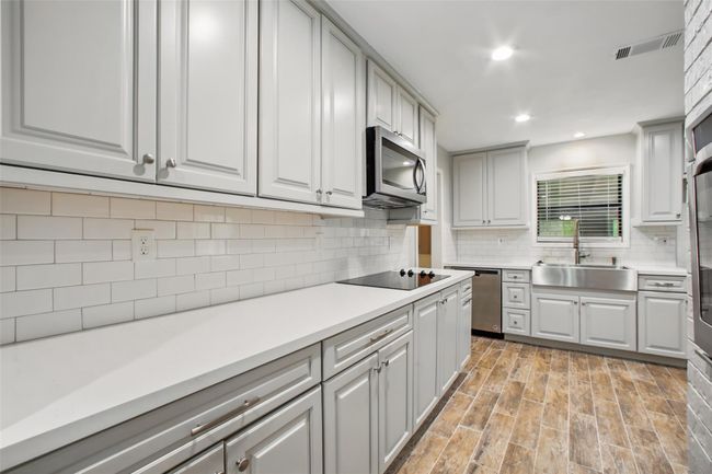 This galley-style kitchen blends classic finishes with modern function—featuring quartz countertops, grey transitional cabinetry, and a white subway tile backsplash that adds timeless character. | Image 9