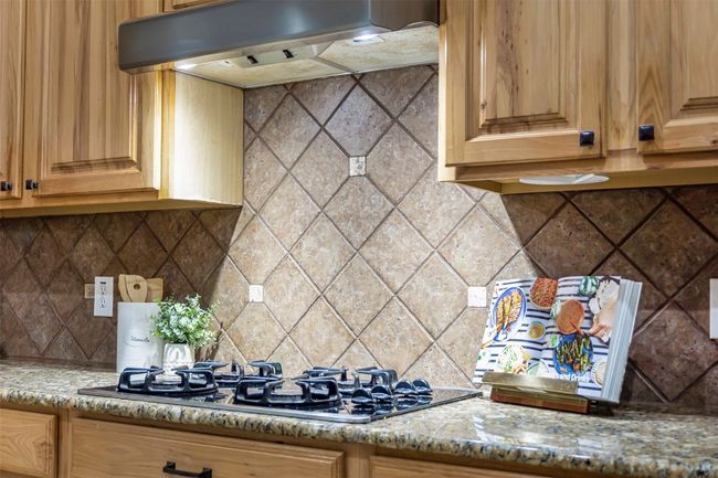 Kitchen featuring black gas stovetop, under cabinet range hood, tasteful backsplash, and light stone countertops | Image 15