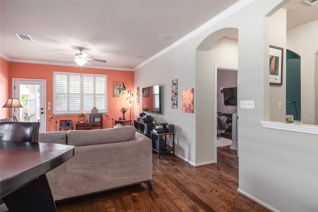 Living area with arched walkways, a ceiling fan, dark wood-style flooring, crown molding, and baseboards | Image 7