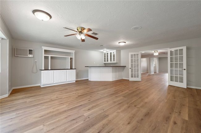 Unfurnished living room with french doors, a ceiling fan, an AC wall unit, light wood finished floors, and a textured ceiling | Image 9