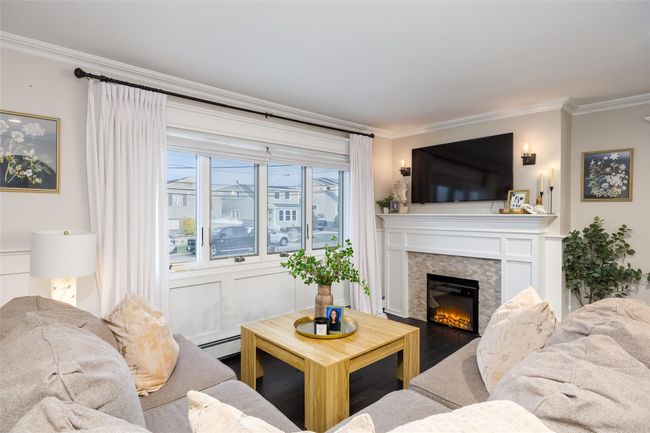 Living room with a baseboard radiator, wood finished floors, a lit fireplace, and ornamental molding | Image 10