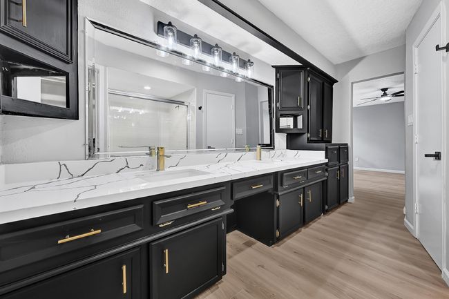 The stunning primary bathroom features a double-sink vanity with dramatic black cabinetry, gold hardware, and elegant quartz countertops. Enhanced lighting and ample storage make this space both luxurious and functional. | Image 28