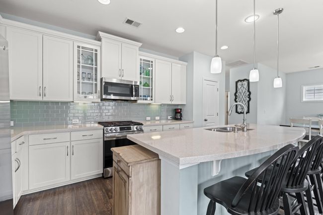 Kitchen with appliances with stainless steel finishes, a sink in the large island, dark wood-style flooring, glass insert cabinets, light stone counters, recessed lighting and under cabinet lighting. | Image 25