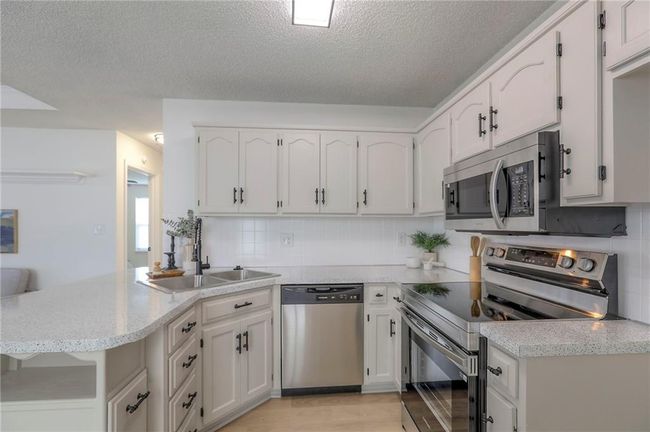 Kitchen with stainless steel appliances, a textured ceiling, a peninsula, tasteful backsplash, and light countertops | Image 8