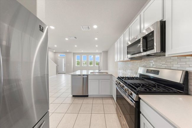 Kitchen with stainless steel appliances, a sink, light tile patterned floors, backsplash, and white cabinetry | Image 11