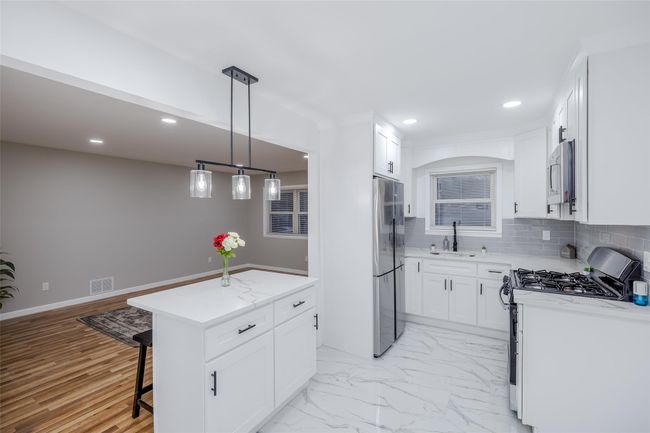 Kitchen featuring white cabinetry, appliances with stainless steel finishes, a center island, decorative light fixtures, and sink | Image 17