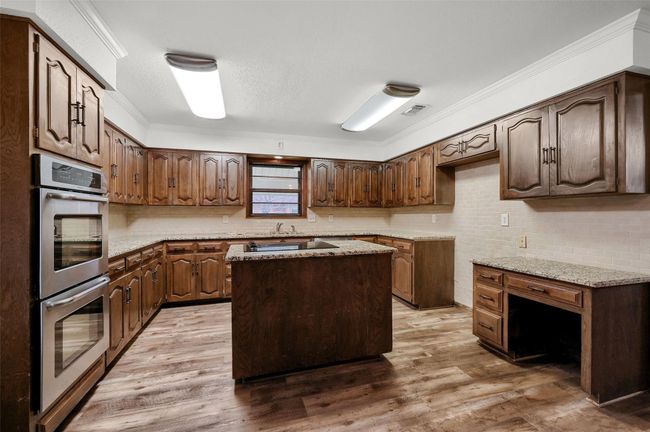 Kitchen featuring stainless steel double oven, tasteful backsplash, wood finished floors, ornamental molding, and a center island | Image 11
