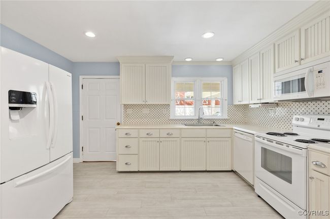 Kitchen featuring white appliances, decorative backsplash, light countertops, light wood finished floors, and a sink | Image 14