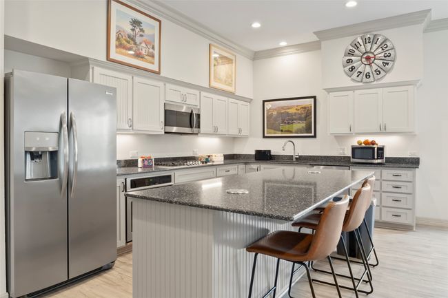 Kitchen featuring a kitchen breakfast bar, ornamental molding, appliances with stainless steel finishes, a center island, and dark stone counters | Image 10