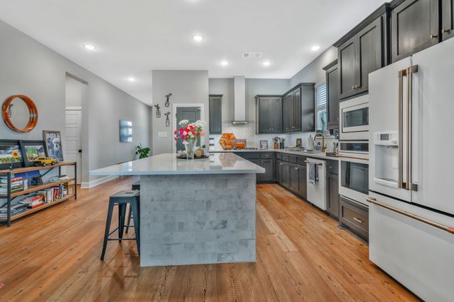 Kitchen with white appliances, a kitchen island, a kitchen bar, wall chimney exhaust hood, and tasteful backsplash | Image 9