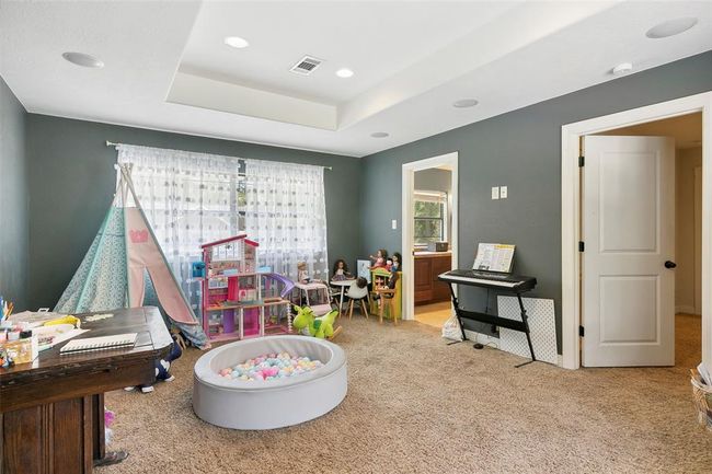 This photo shows a cozy playroom with carpeted floors, featuring a play tent, toy storage, and a ball pit. It's brightened by natural light from a large window with sheer curtains. There's also a keyboard against a gray wall, and an open doorway leading to another room. Ideal for a child's play area or creative space. | Image 39