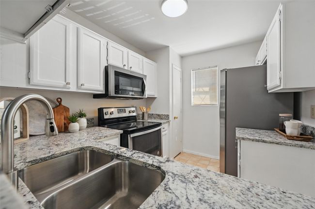Kitchen featuring a sink, light stone countertops, white cabinetry, and stainless steel appliances | Image 5