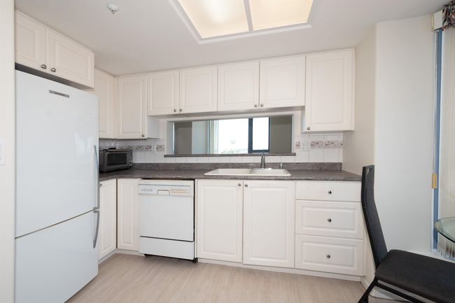 Kitchen featuring white appliances, dark countertops, a sink, and white cabinetry | Image 17