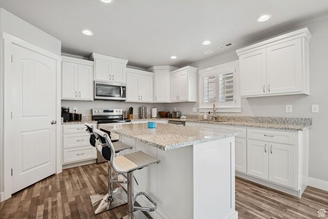 Kitchen with appliances with stainless steel finishes, wood finished floors, white cabinetry, a kitchen island, and a breakfast bar area | Image 9