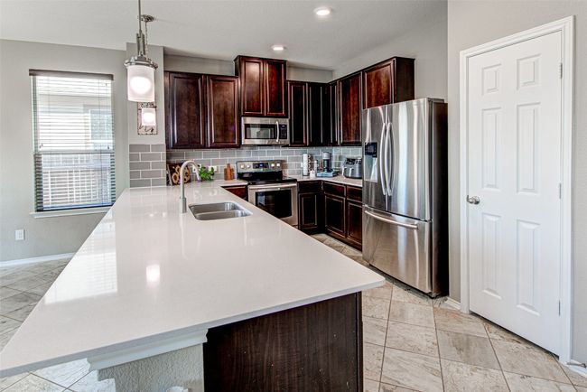 Kitchen with stainless steel appliances, a peninsula, a sink, backsplash, and light countertops | Image 10