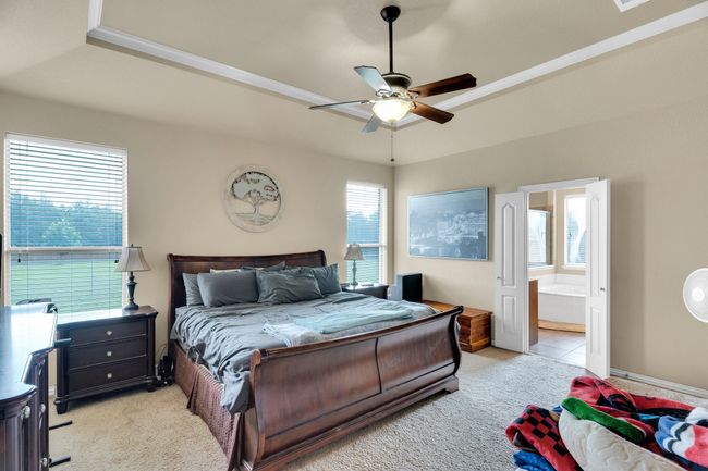 Bedroom featuring light carpet, ensuite bathroom, ceiling fan, and a tray ceiling | Image 10