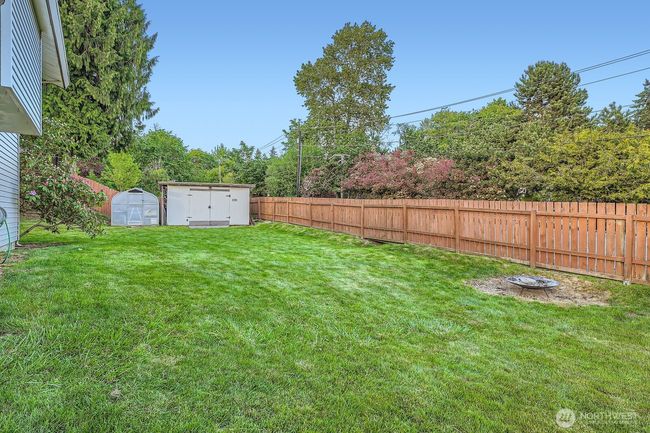 Side yard has firepit area, a shed, greenhouse and fencing. | Image 35