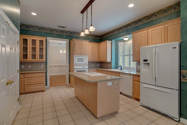 Kitchen with white appliances, wallpapered walls, light brown cabinetry, light countertops, and light tile patterned floors | Image 11