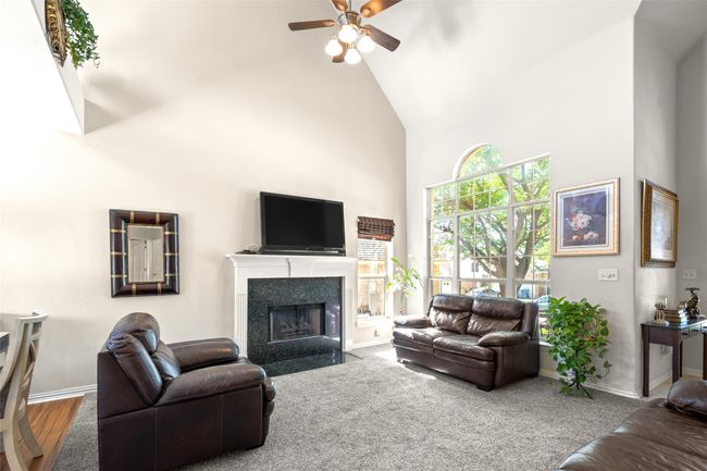 Living room with high vaulted ceiling, ceiling fan, baseboards, and a fireplace with flush hearth | Image 9