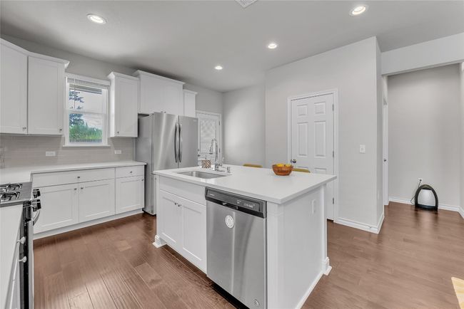 Kitchen with appliances with stainless steel finishes, a sink, dark wood finished floors, a center island with sink, and white cabinets | Image 7