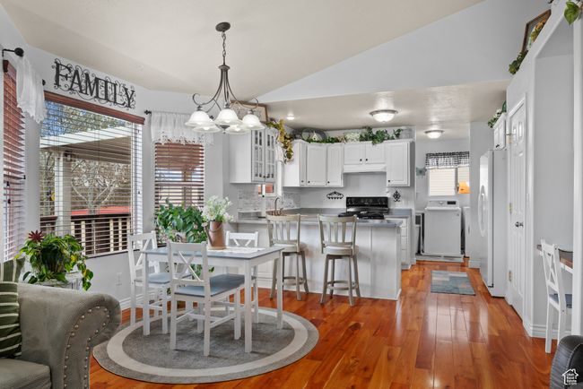 Dining room featuring a notable chandelier, washer / dryer, vaulted ceiling, and light wood-type flooring | Image 7