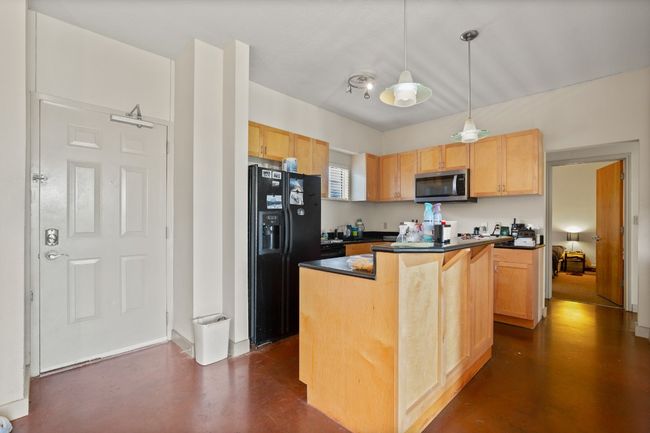 Kitchen featuring stainless steel microwave, black fridge with ice dispenser, dark countertops, and concrete flooring | Image 4