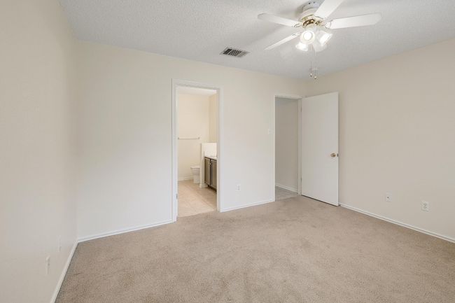 Unfurnished bedroom featuring light colored carpet, ensuite bathroom, baseboards, a textured ceiling, and a ceiling fan | Image 15