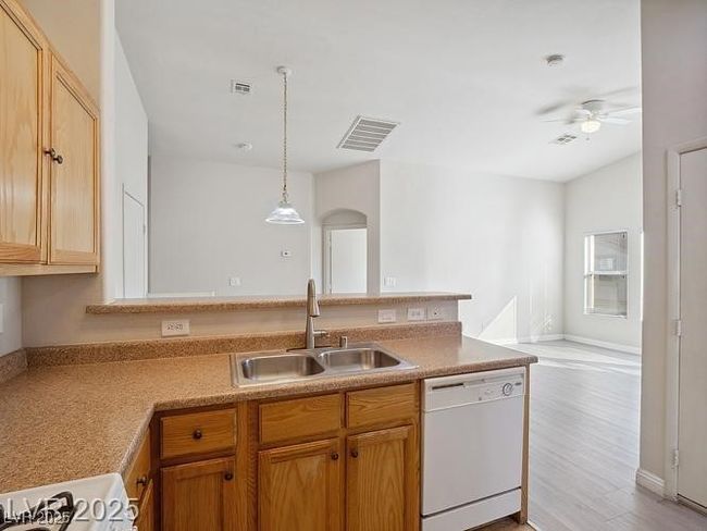 Kitchen with white dishwasher, a peninsula, light countertops, open floor plan, and decorative light fixtures | Image 8