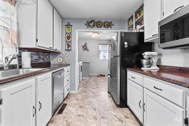 Kitchen with stainless steel appliances, white cabinetry, decorative backsplash, open shelves, and washing machine and dryer | Image 15